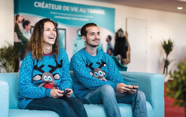 Dos empleados jugando a videojuegos con jerséis de Navidad.
