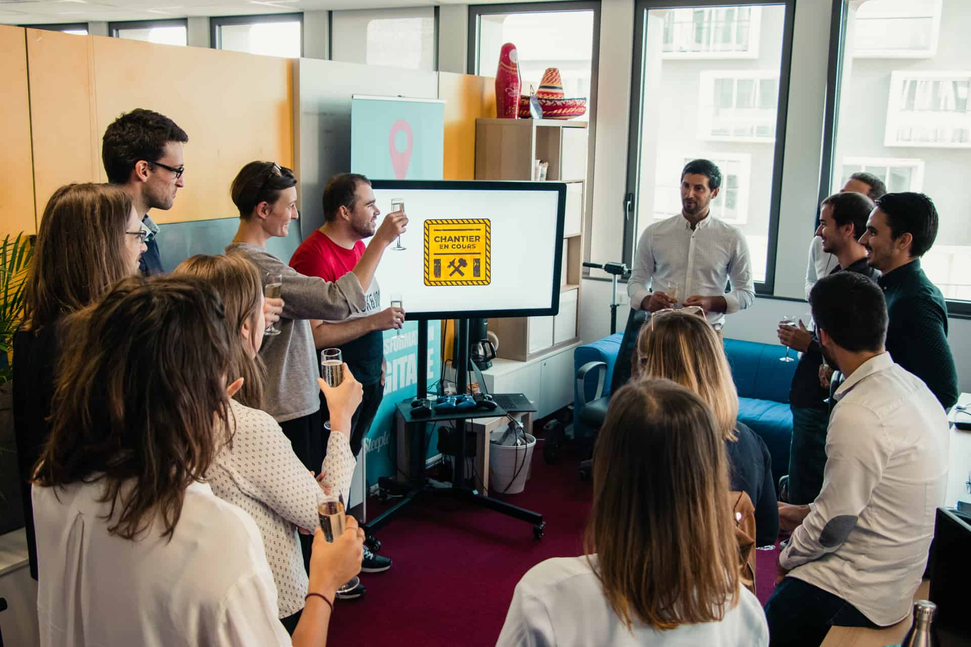 Empleados teniendo una reunión alrededor de la pantalla de Steeple en la zona de descanso con el CEO de Steeple Jean-Baptiste